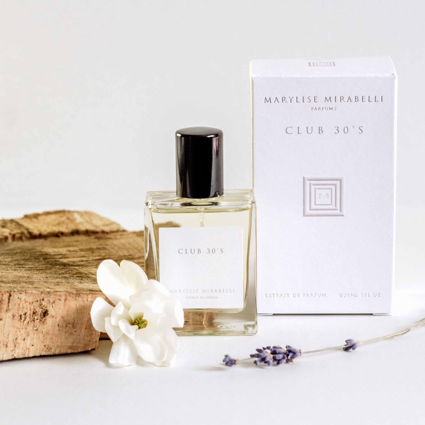 Petit flacon de parfum posé sur une table blanche à côté de sa boite. Le flacon de 30ml est rectangulaire avec une étiquette blanche, l'inscription Club 30's et un bouchon noir brillant. La boite est blanche avec le logo carré au centre et les inscriptions Marylise Mirabelli parfums et Club 30's en haut. Une fleur blanche et un brin de lavande son posés délicatement à côté du flacon qui est adossé sur un morceau de bois clair.