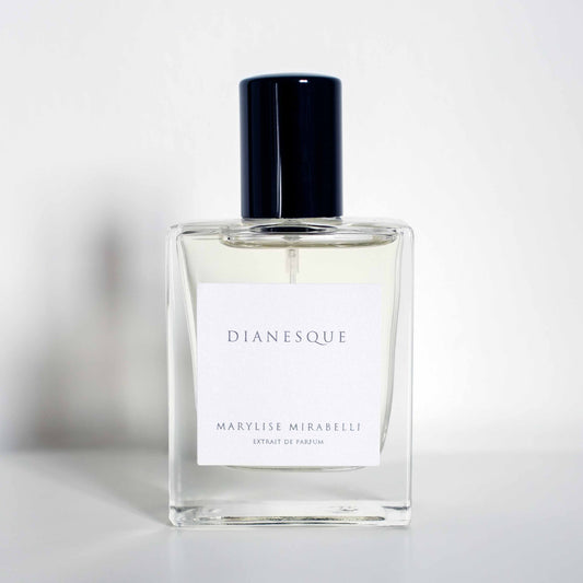Flacon sobre et rectangulaire avec étiquette blanche et bouchon noir brillant, posé sur un fond blanc. Sur l'étiquette il est inscrit Dianesque en haut et Marylise Mirabelli Extrait de parfum en bas.